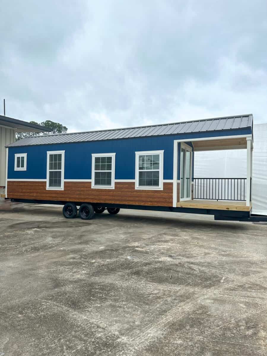Tiny house on wheels with covered porch and modern blue exterior.