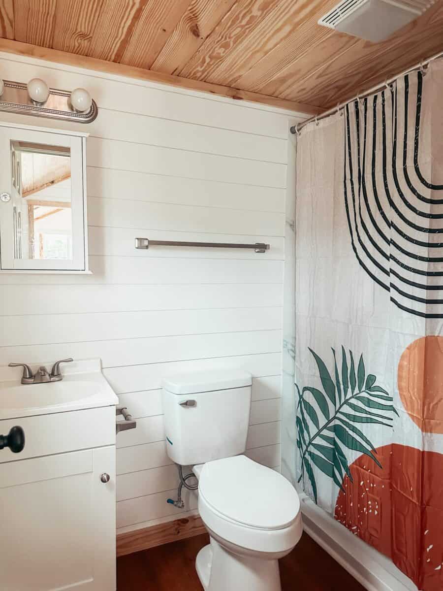 Bathroom in tiny house with wooden ceiling and tropical-themed shower curtain.