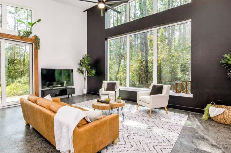 Cozy living room with large windows showcasing lush forest views in a modern Florida pine cabin.