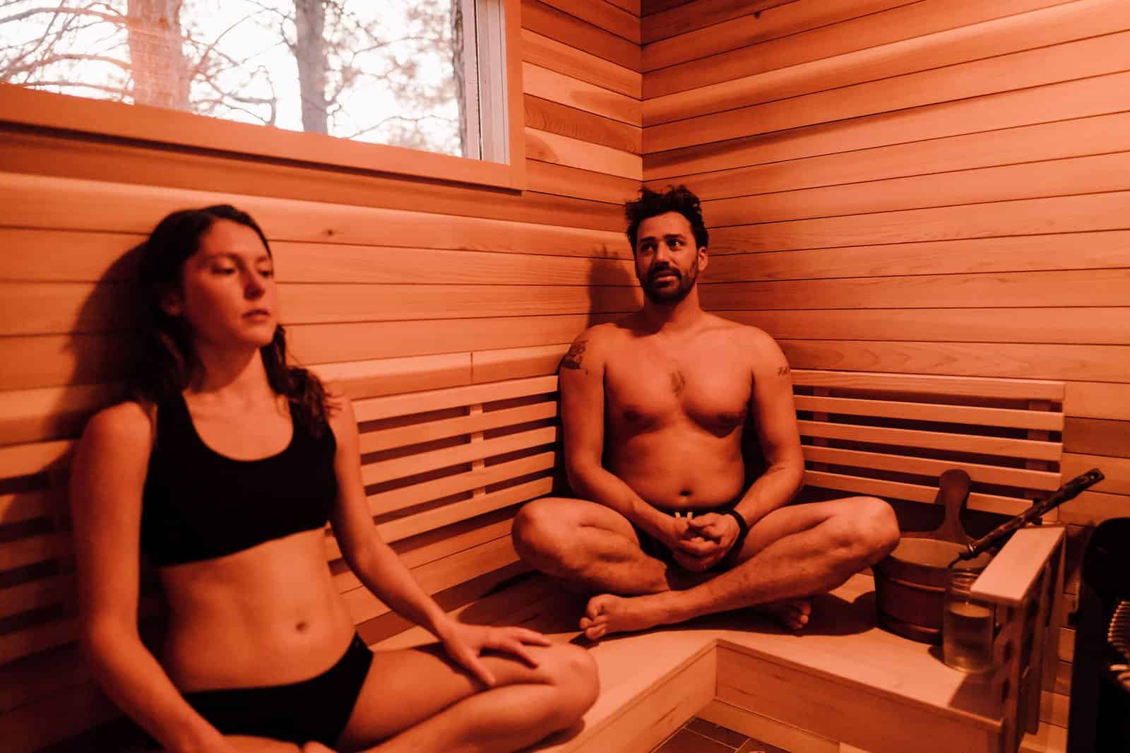 Two people relaxing on the cedar benches inside the warmly lit River West sauna