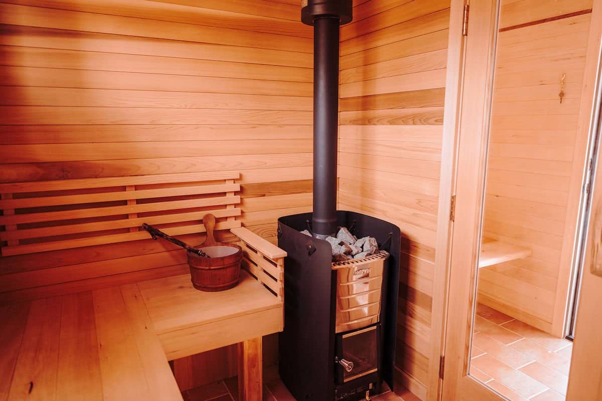 Interior of the River West sauna with cedar benches and a wood-fired Harvia stove topped with sauna rocks