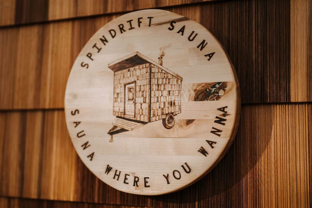 A wood-burned Spindrift Sauna medallion reading Sauna Where You Wanna on the River West's cedar shingles