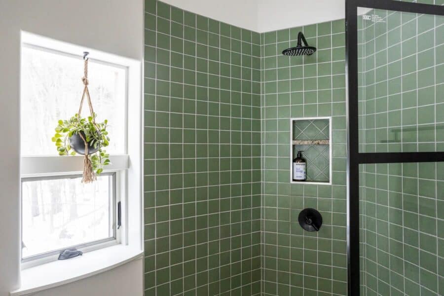 Green tiled shower with a window and hanging plant in a tiny home bathroom.