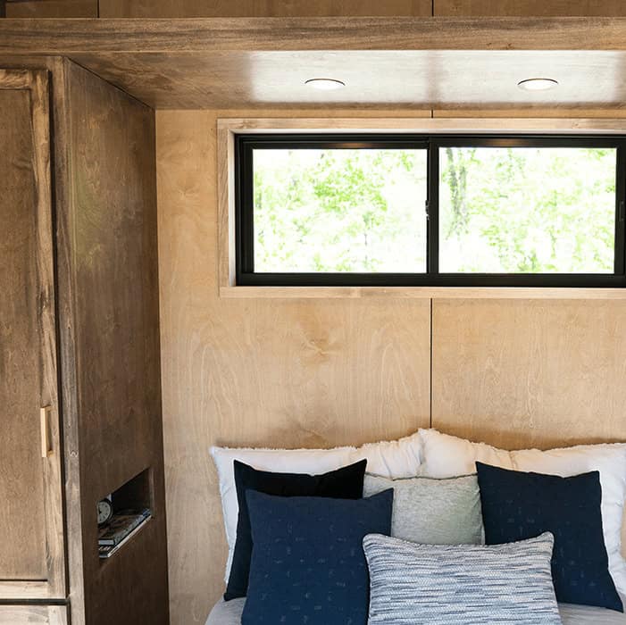 Compact tiny house bedroom with large window and cozy bedding.