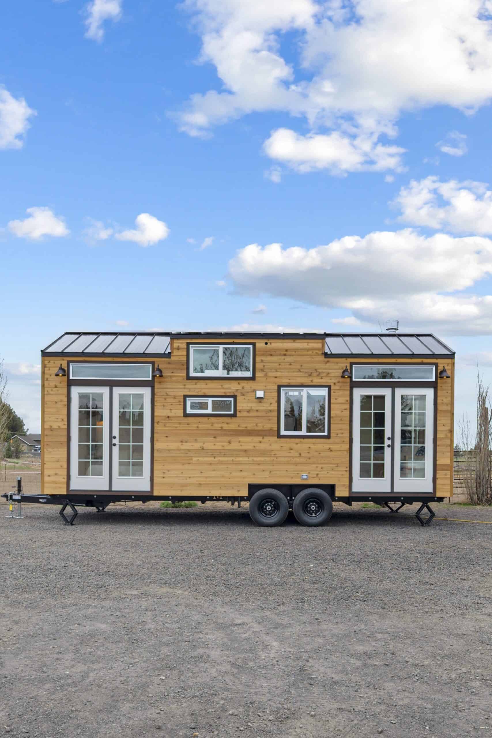 End view of the Shasta tiny house showing its cedar siding, dormer roof, and French doors at both ends
