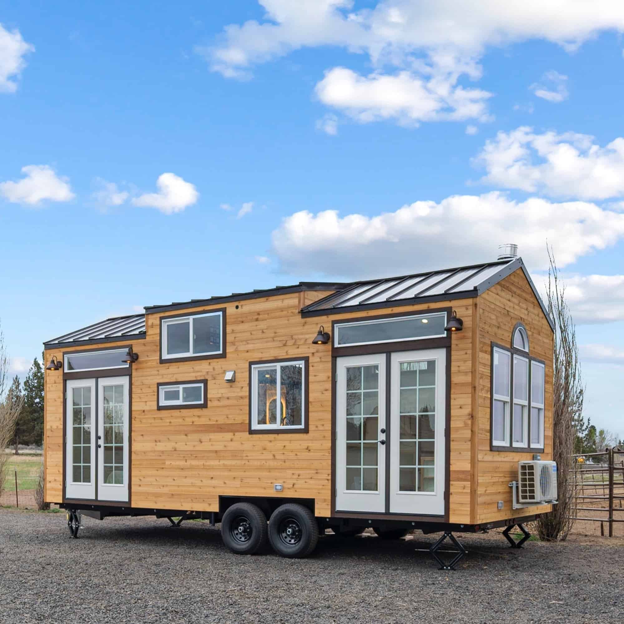 The Shasta tiny house by Spindrift Homes with cedar siding, a dormer metal roof, and French doors on a double-axle trailer