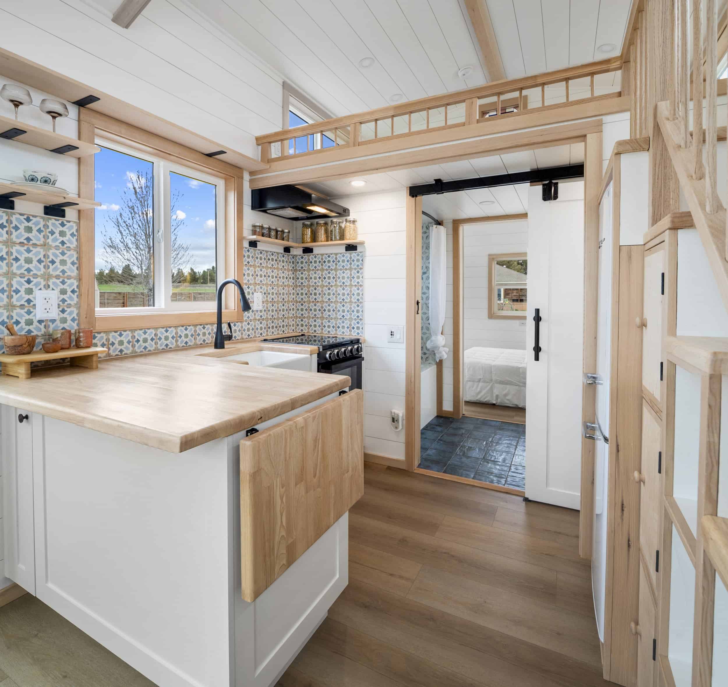 The Shasta kitchen with a butcher block peninsula, farmhouse sink, gas range, patterned tile backsplash, and a barn door to the bedroom