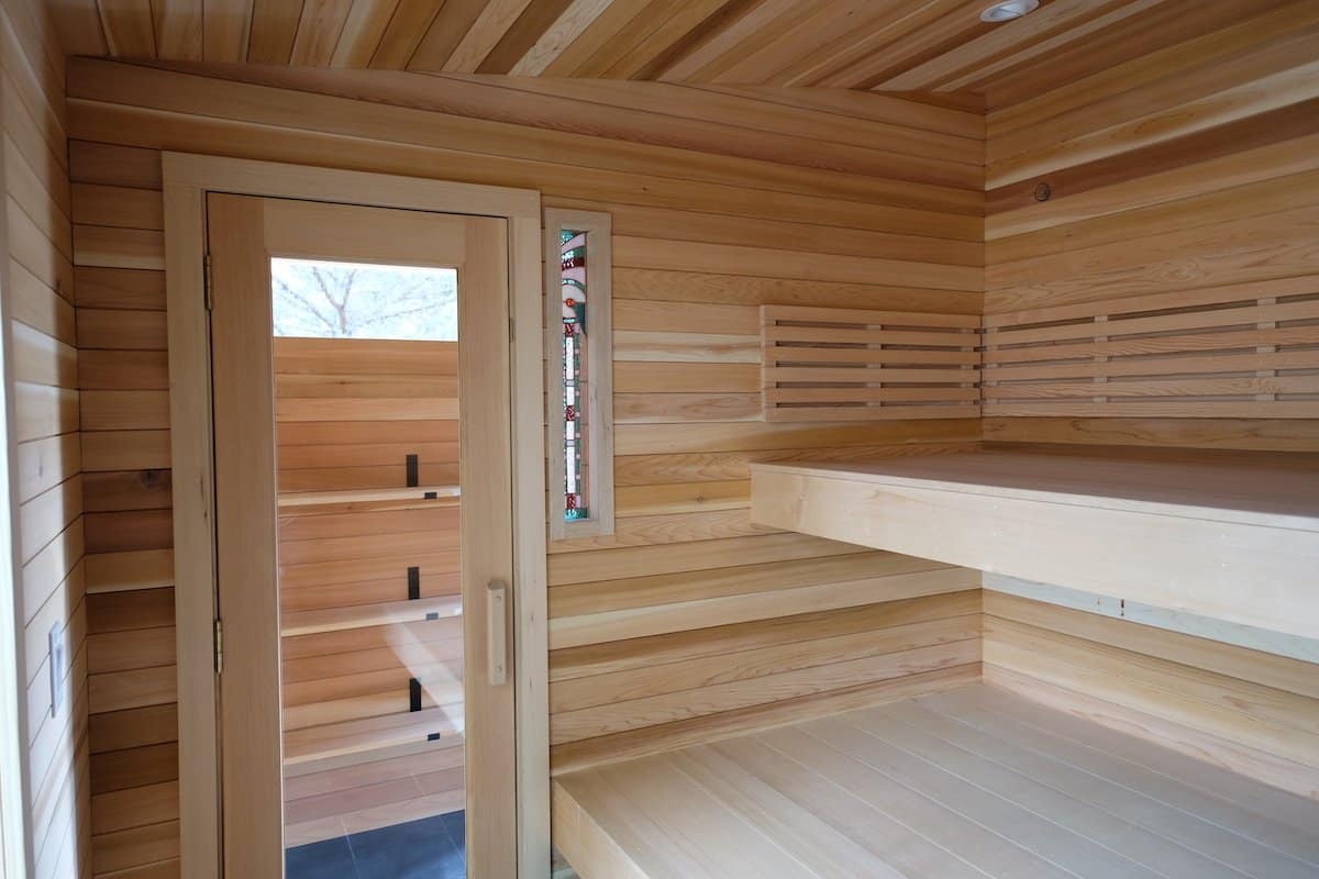The Silverado sauna's tiered cedar benches, slat backrest, glass door, and a custom stained-glass accent window