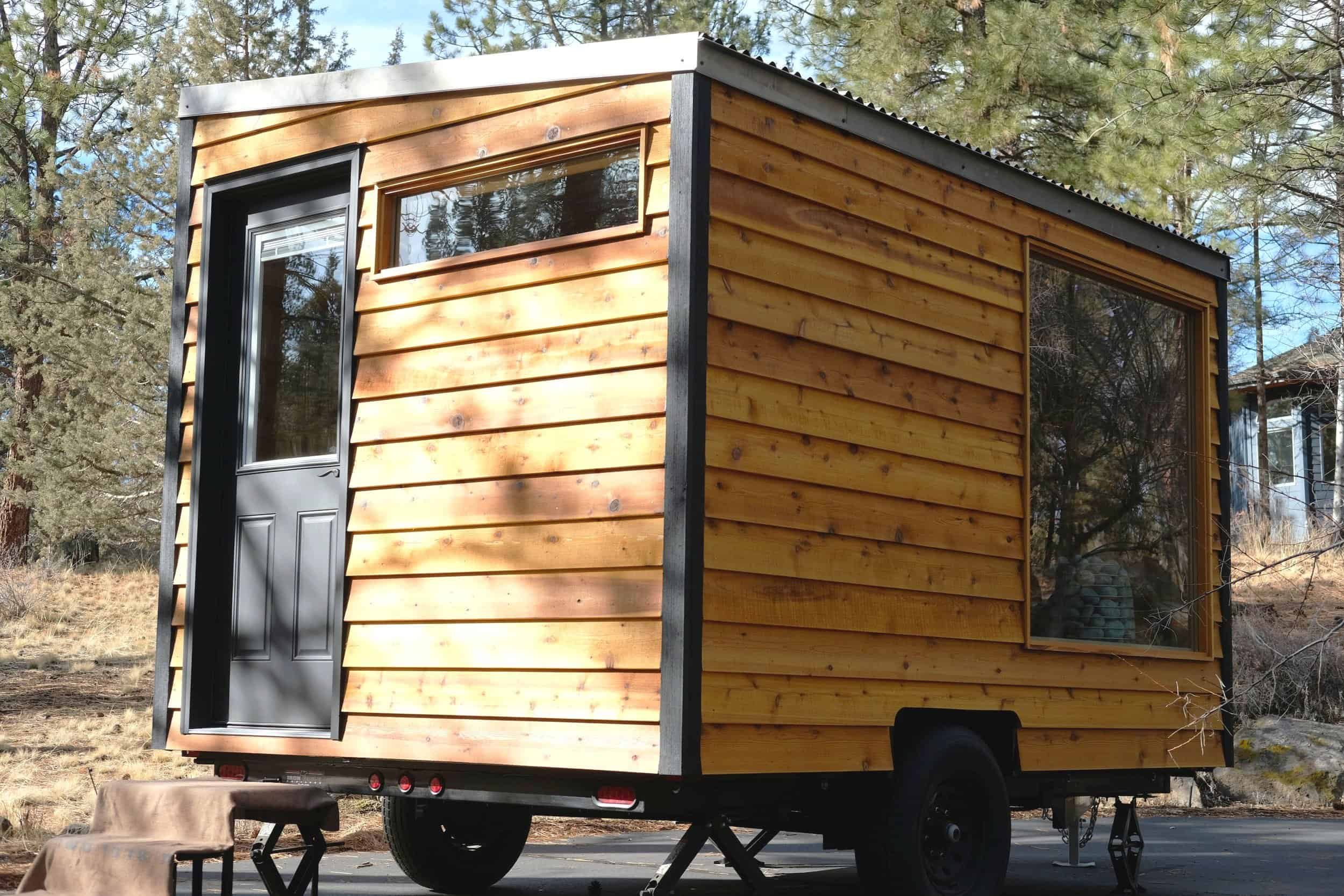 The Silverado mobile sauna by Spindrift Homes with cedar shiplap siding and a slanted metal roof on a trailer in the pines