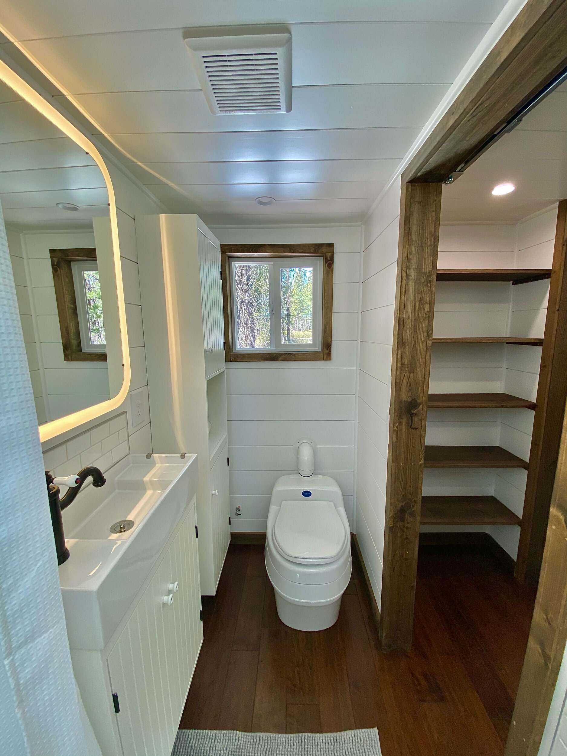 The Sonoma bathroom with a vanity, backlit mirror, composting toilet, window, and open wood shelving