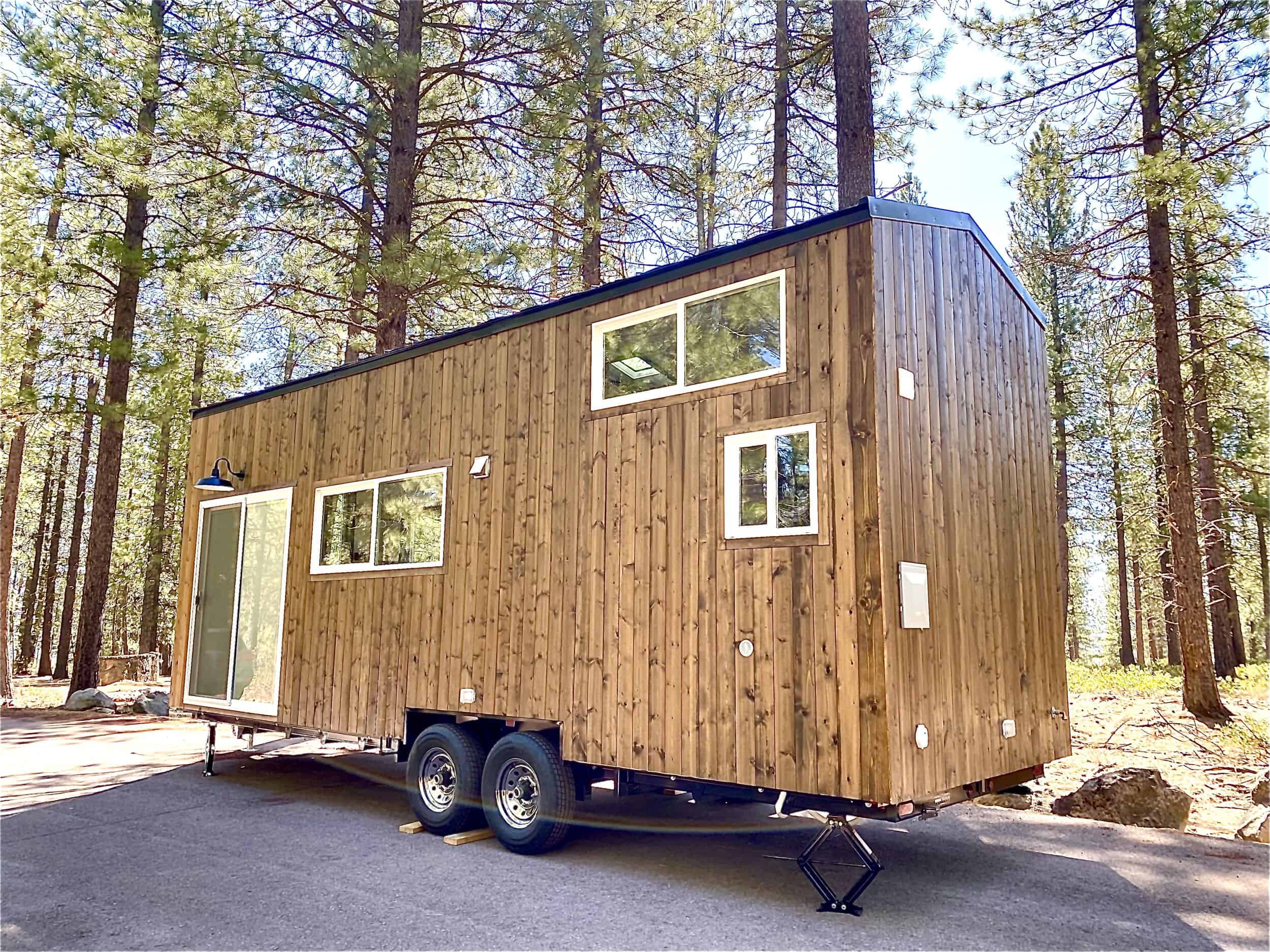 The Sonoma tiny house by Spindrift Homes with wood siding and a metal roof on a double-axle trailer in a pine forest