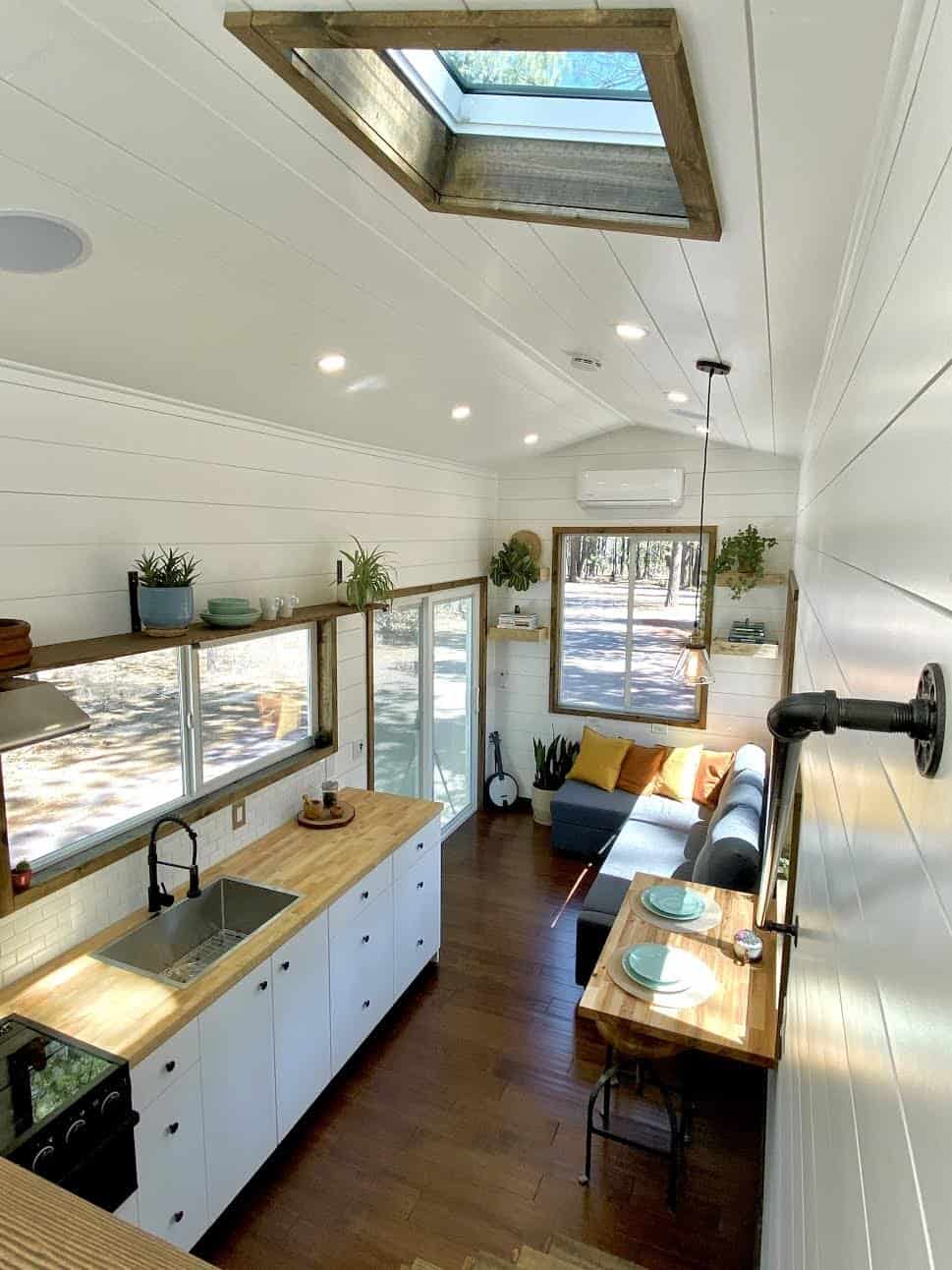 The Sonoma living room with a gray L-shaped sofa bed, yellow and orange pillows, and forest views through large windows