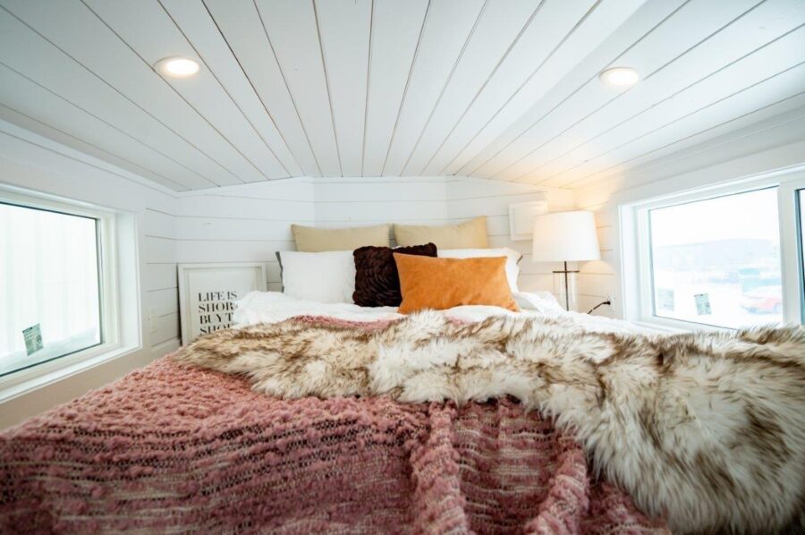 Bright and inviting tiny house bedroom with large windows and soft bedding. Perfect for small space.
