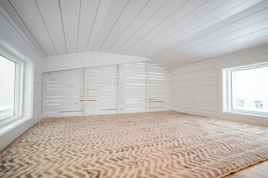 Bright and airy tiny house bedroom with white shiplap walls and large windows.