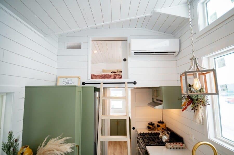 Bright tiny house with white walls and green accents, featuring a compact kitchen and loft space.