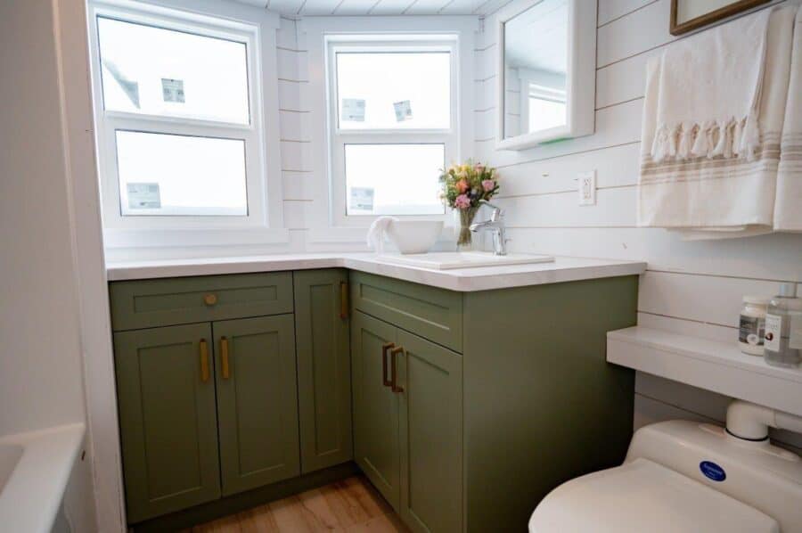 Cozy tiny house bathroom featuring green cabinets and natural light from multiple windows.