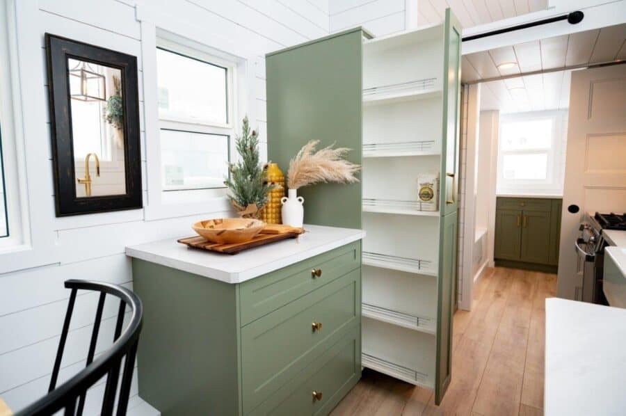 Bright tiny house kitchen with green cabinetry and open shelving.