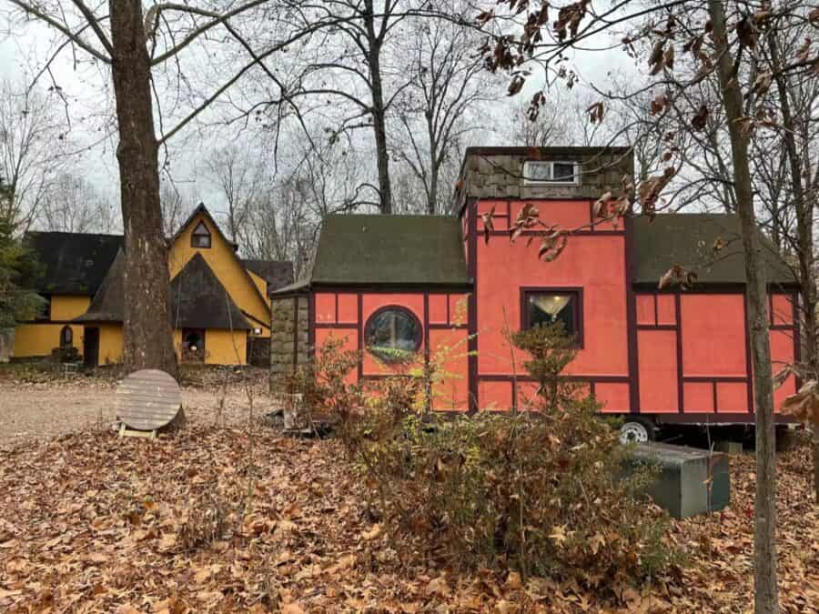 Tiny house in a forest setting with colorful exterior walls and small windows.