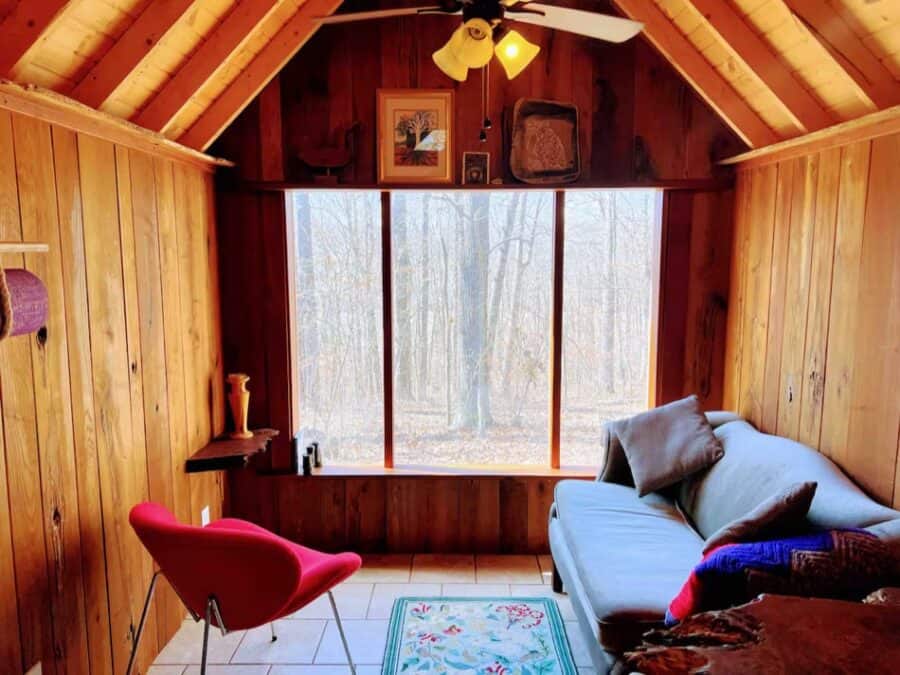 Charming tiny house interior with wooden walls and large window overlooking forest scenery.