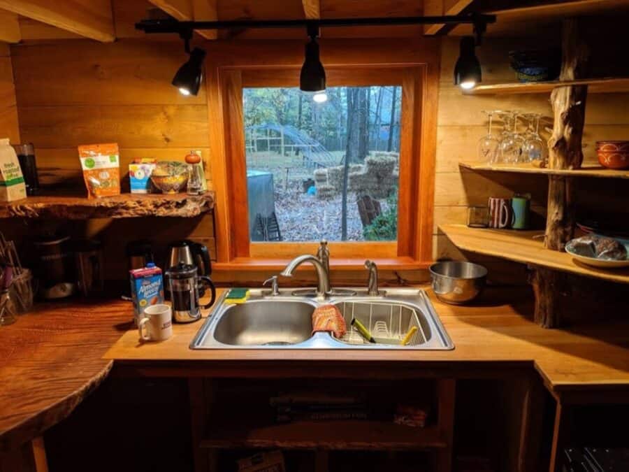Compact tiny house kitchen with rustic wood accents and a scenic forest view through the window.
