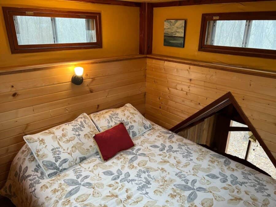 Charming tiny house bedroom with wood paneling and natural light at the Forest Retreat in Illinois.