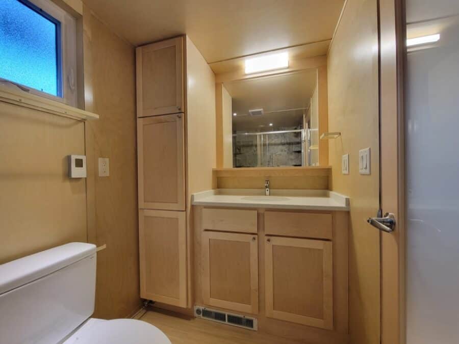 Compact tiny house bathroom with wooden cabinets and a mirror.