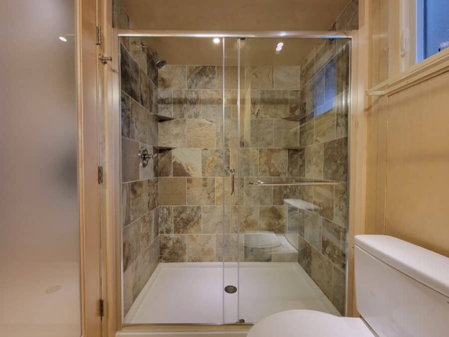 Bathroom in a tiny house with natural stone tile walls and a glass shower enclosure.