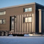 Compact modern tiny house with sleek brown exterior and multiple windows, built on a trailer for mob.