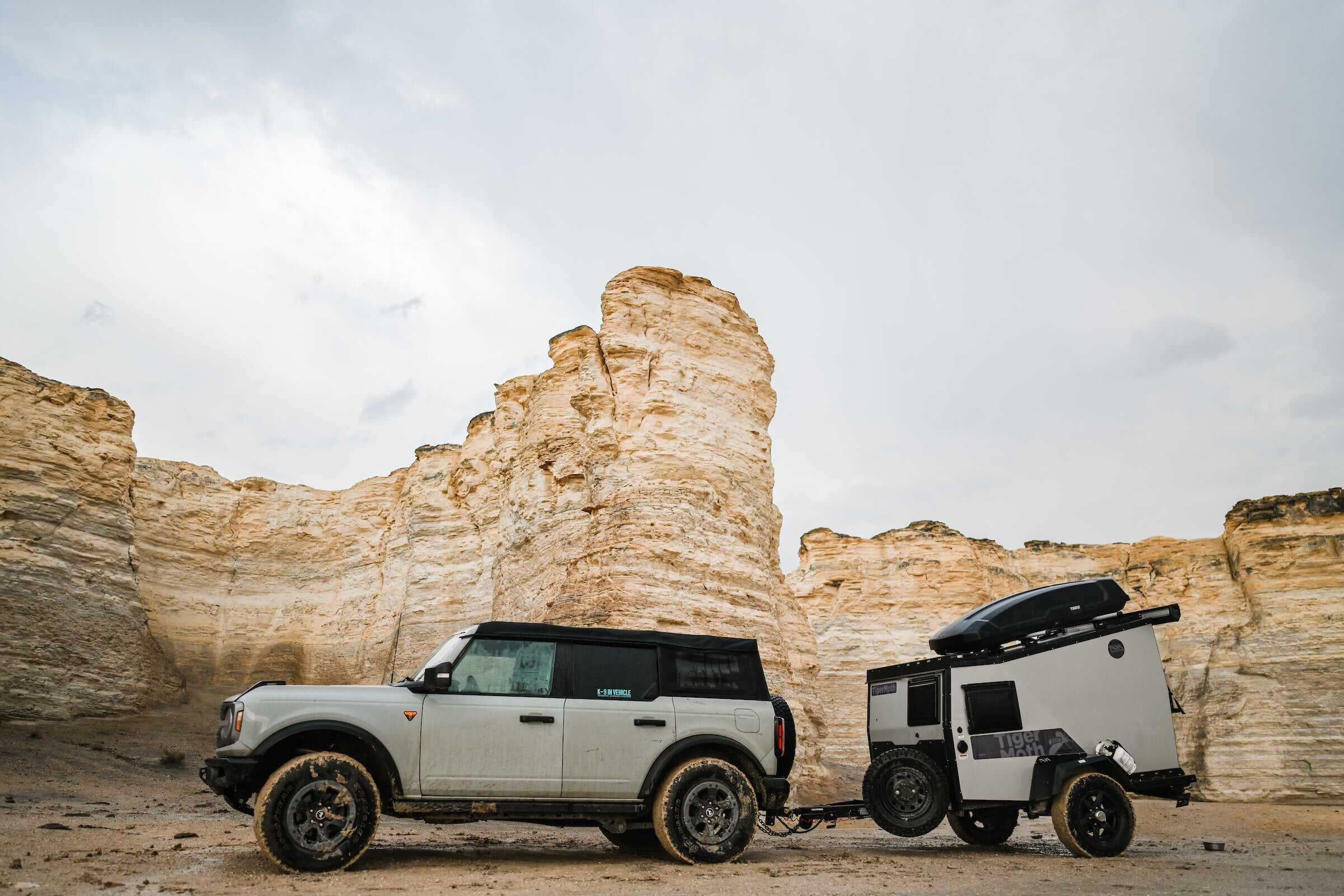 Off-road vehicle towing a compact tiny house trailer in a rugged canyon landscape.
