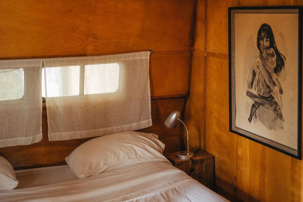 Private bedroom inside Tin Poppy Cabin with a queen bed, warm plywood walls and linen curtains