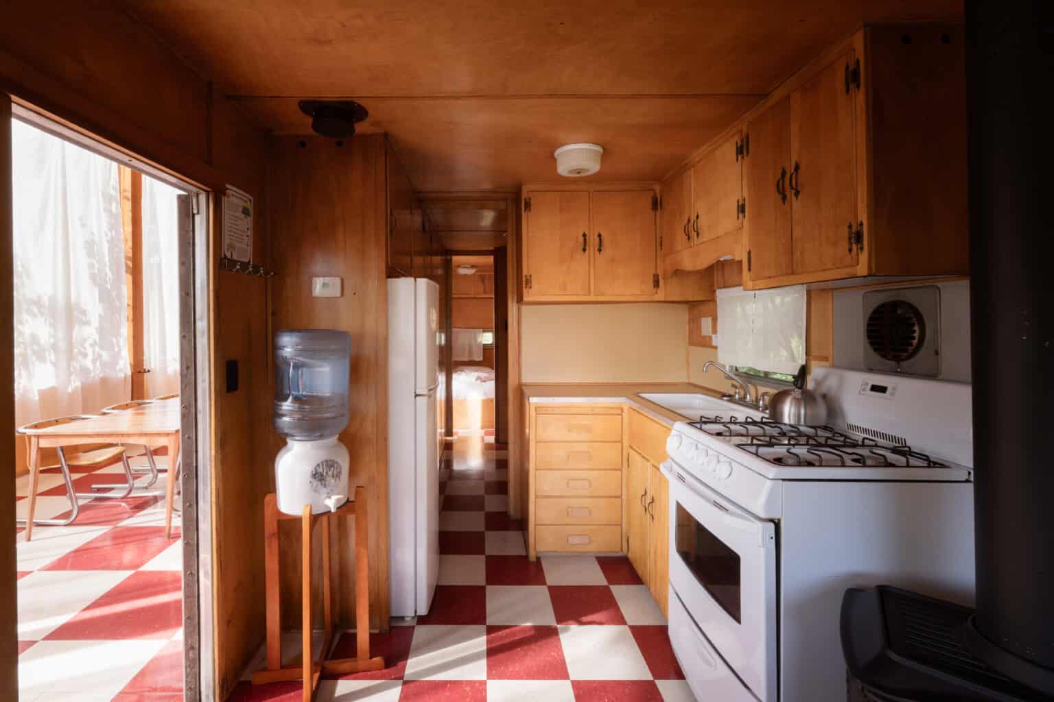 The original 1953 galley kitchen inside Tin Poppy Cabin, with birch cabinets, gas range and red checkerboard floor