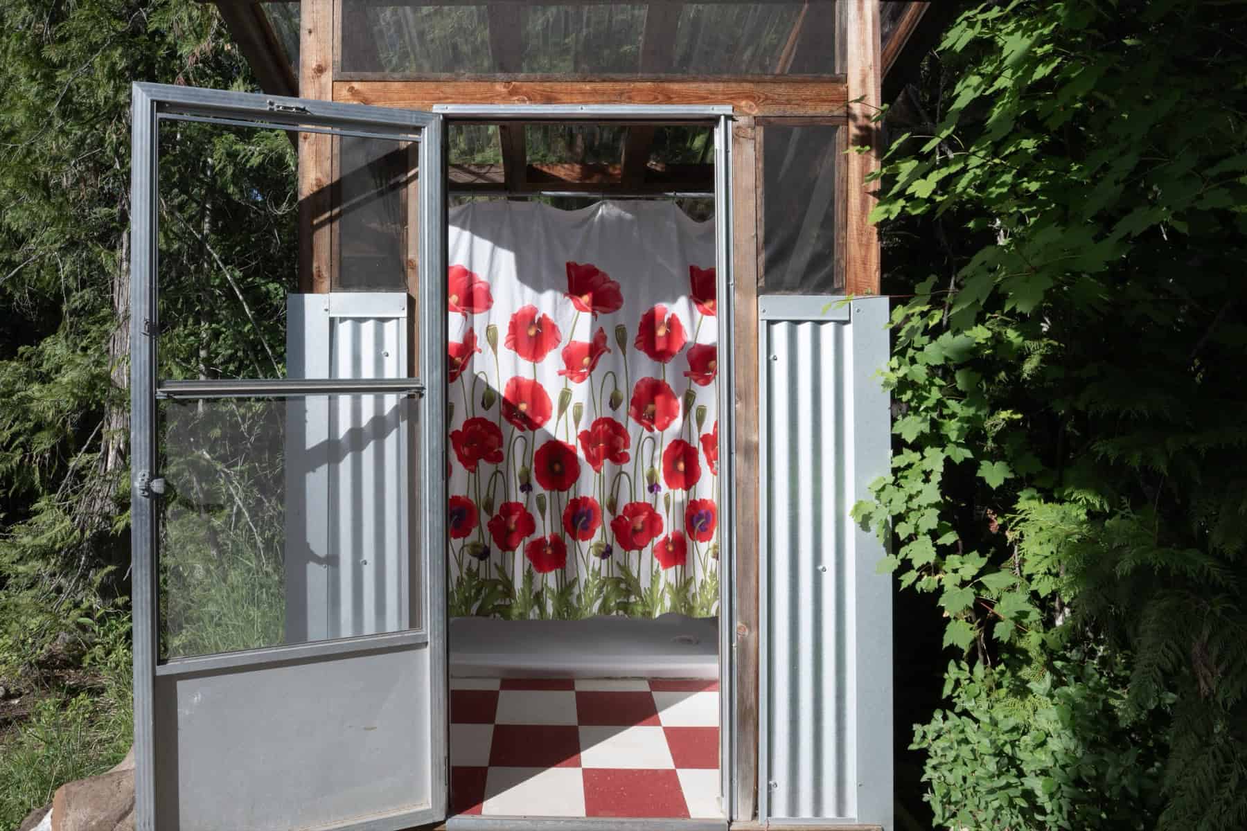 The private outdoor shower at Tin Poppy Cabin, with a poppy-print curtain and red checkerboard floor