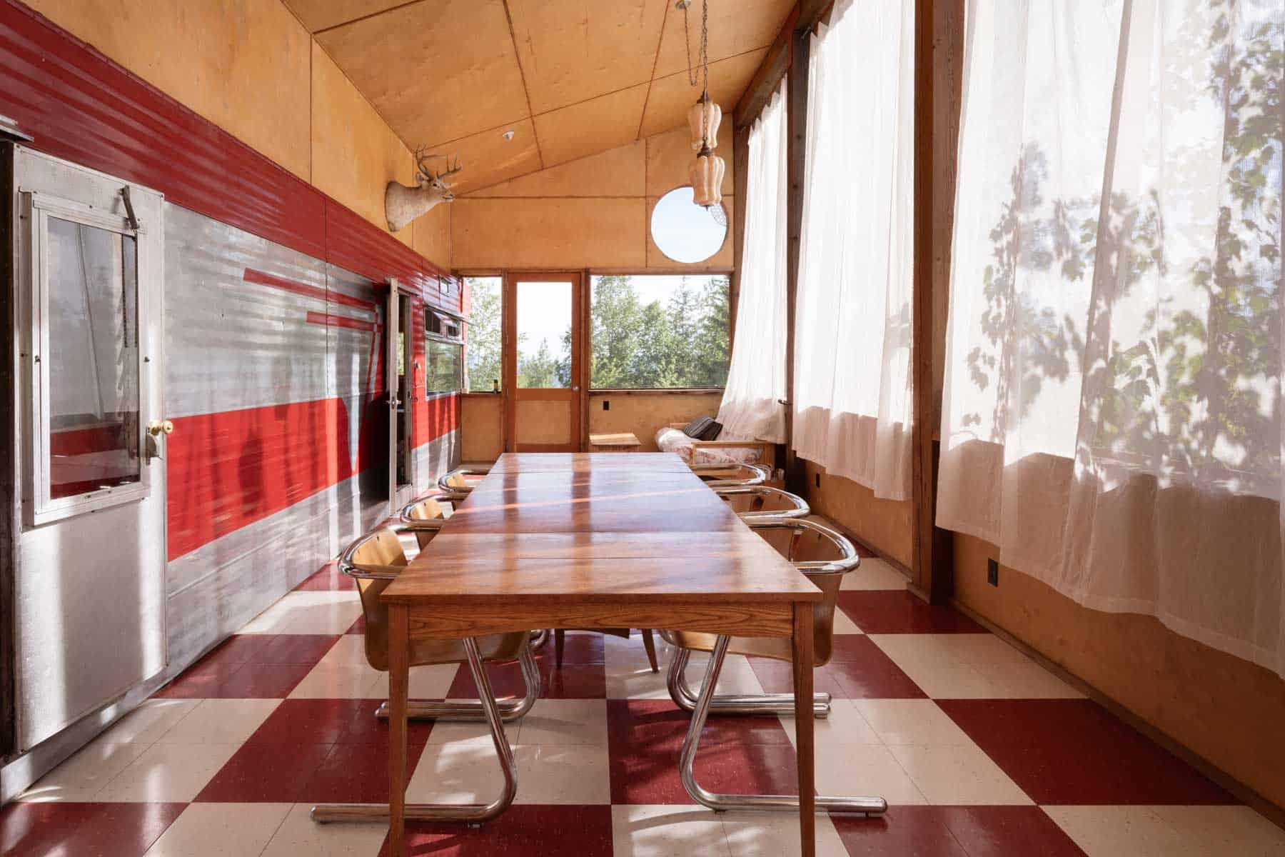 Screened dining room at Tin Poppy Cabin with the vintage trailer's red and aluminum flank serving as an interior wall