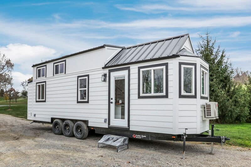 Compact tiny house on wheels with sleek white exterior and large windows for natural light.