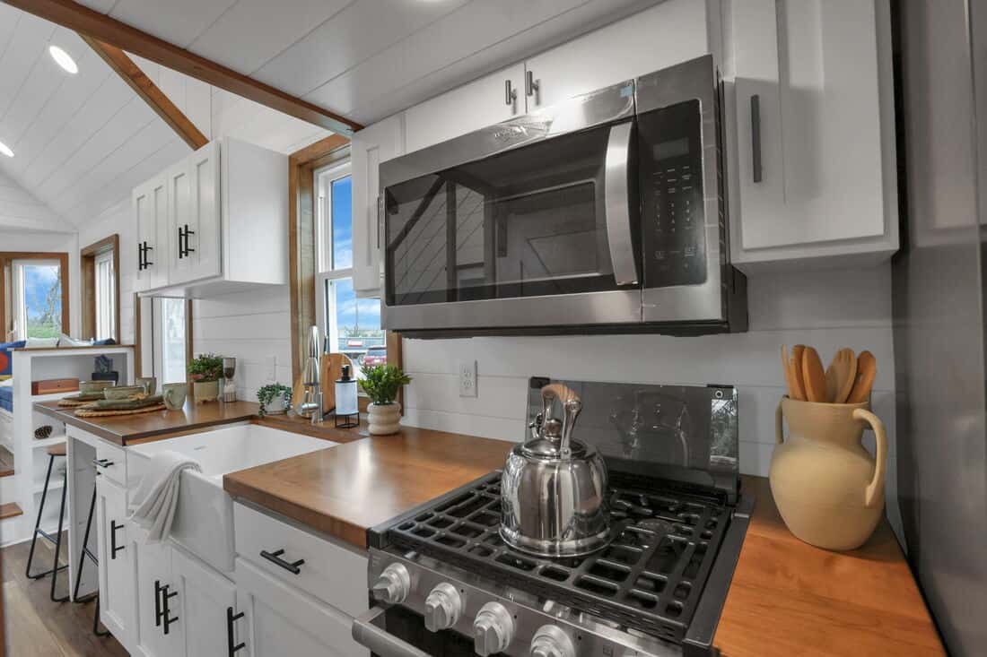 Modern tiny house kitchen with microwave, stove, and wooden countertops.