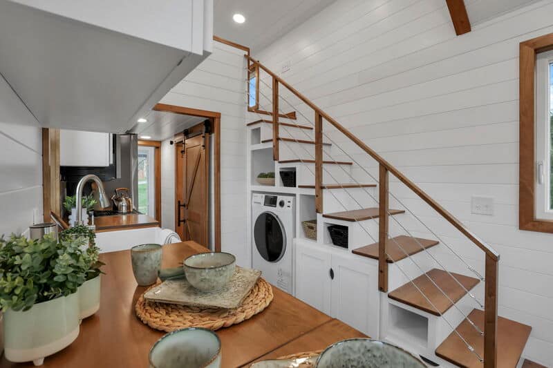 Tiny house interior with wooden stairs and laundry area under the staircase.