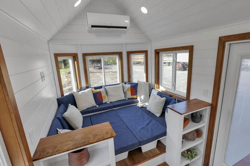 Compact tiny house interior with cozy corner seating and large windows.