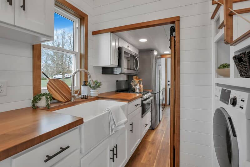 Bright tiny house kitchen with white cabinets and wooden countertops.