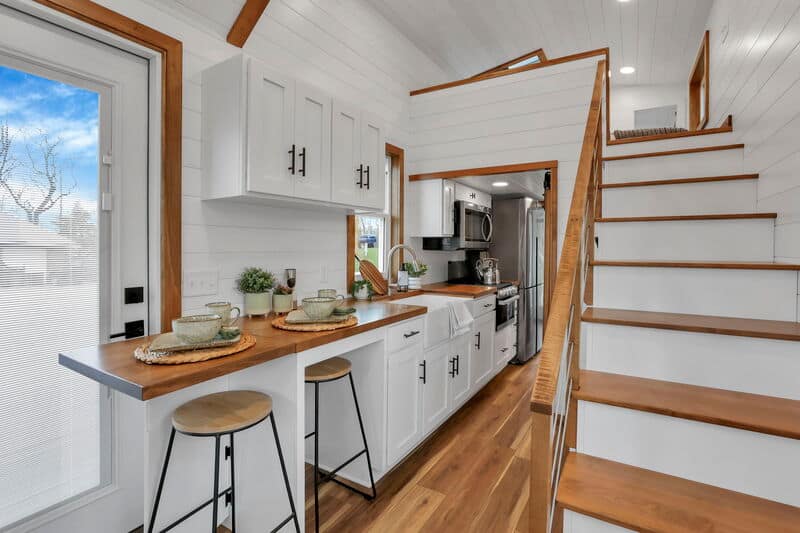Cozy tiny house kitchen with staircase and natural light.
