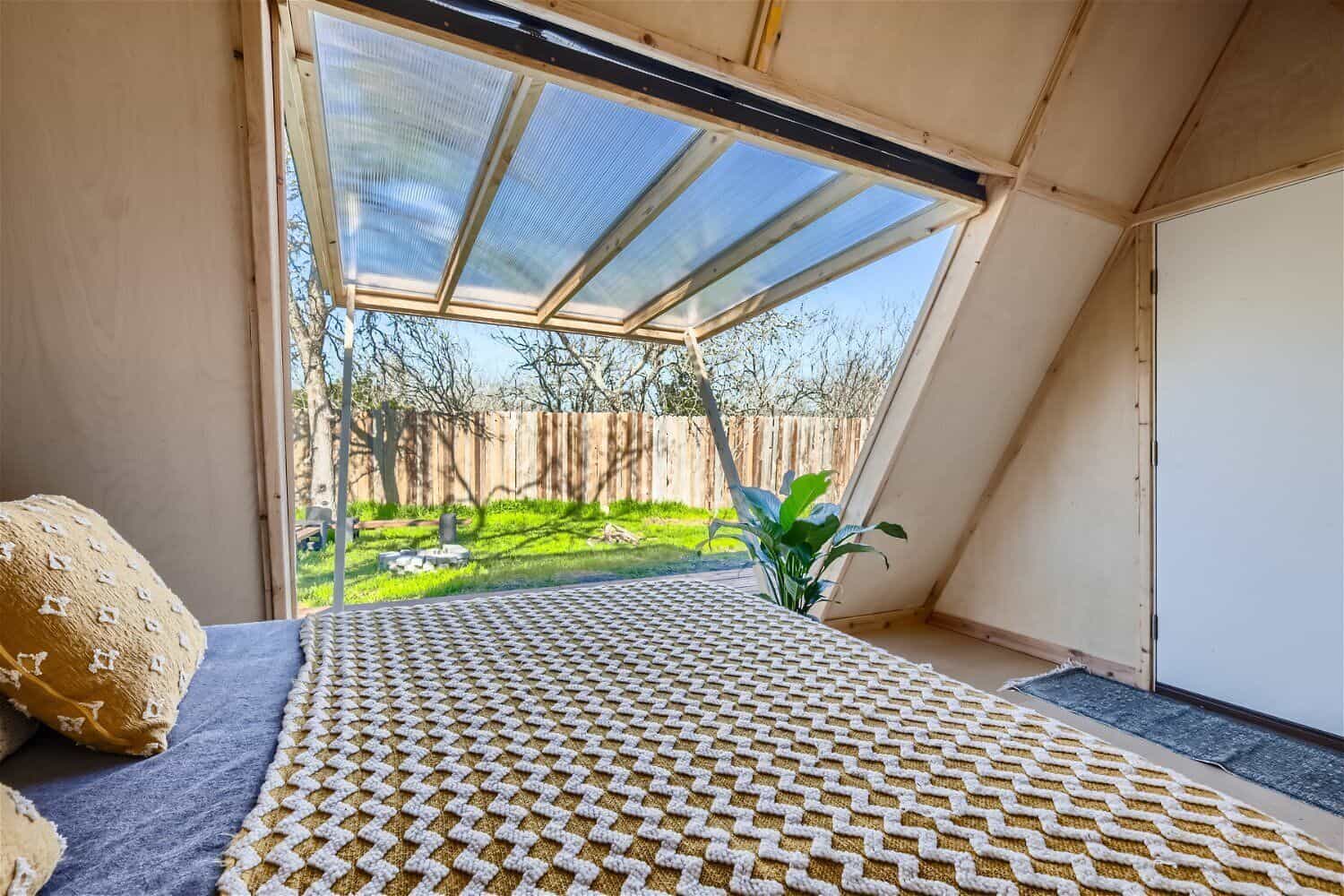 View from the bed inside the A-frame cabin looking out through translucent panels to fire pit and yard