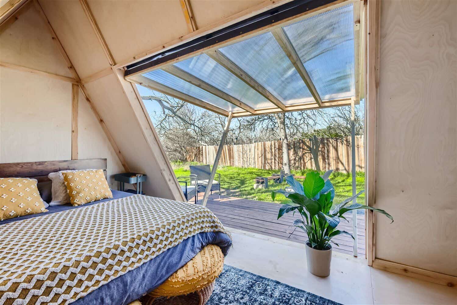 A-frame cabin bedroom looking out through open wall to deck and green Texas countryside