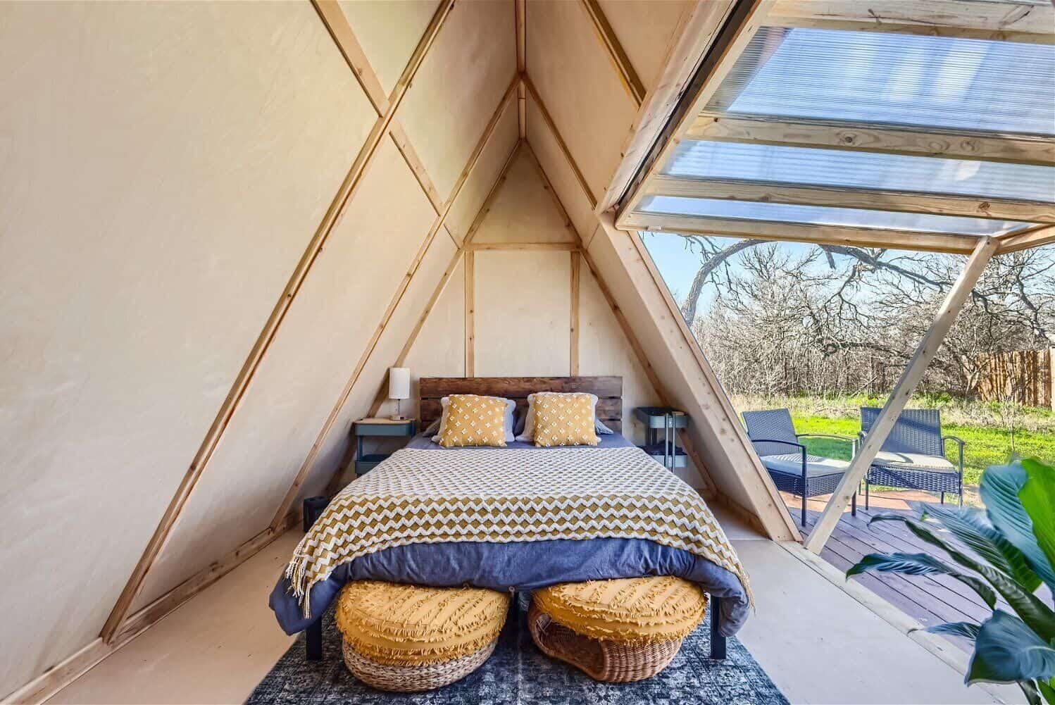Cozy A-frame cabin bedroom with wicker poufs, boho bedding, and view to outdoor deck