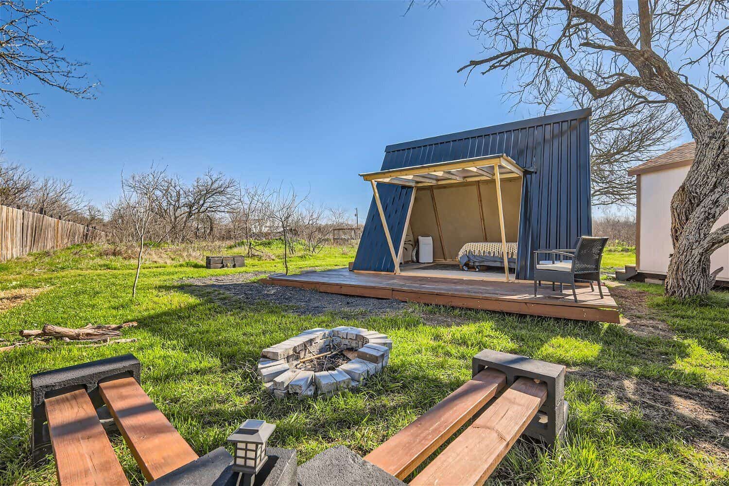 Stone fire pit with wood benches and tiny A-frame cabin on 5 acres of open Texas countryside