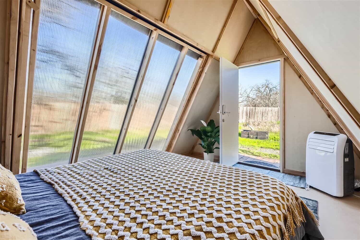 Light-filled A-frame cabin interior with translucent wall panels and queen bed near Austin Texas