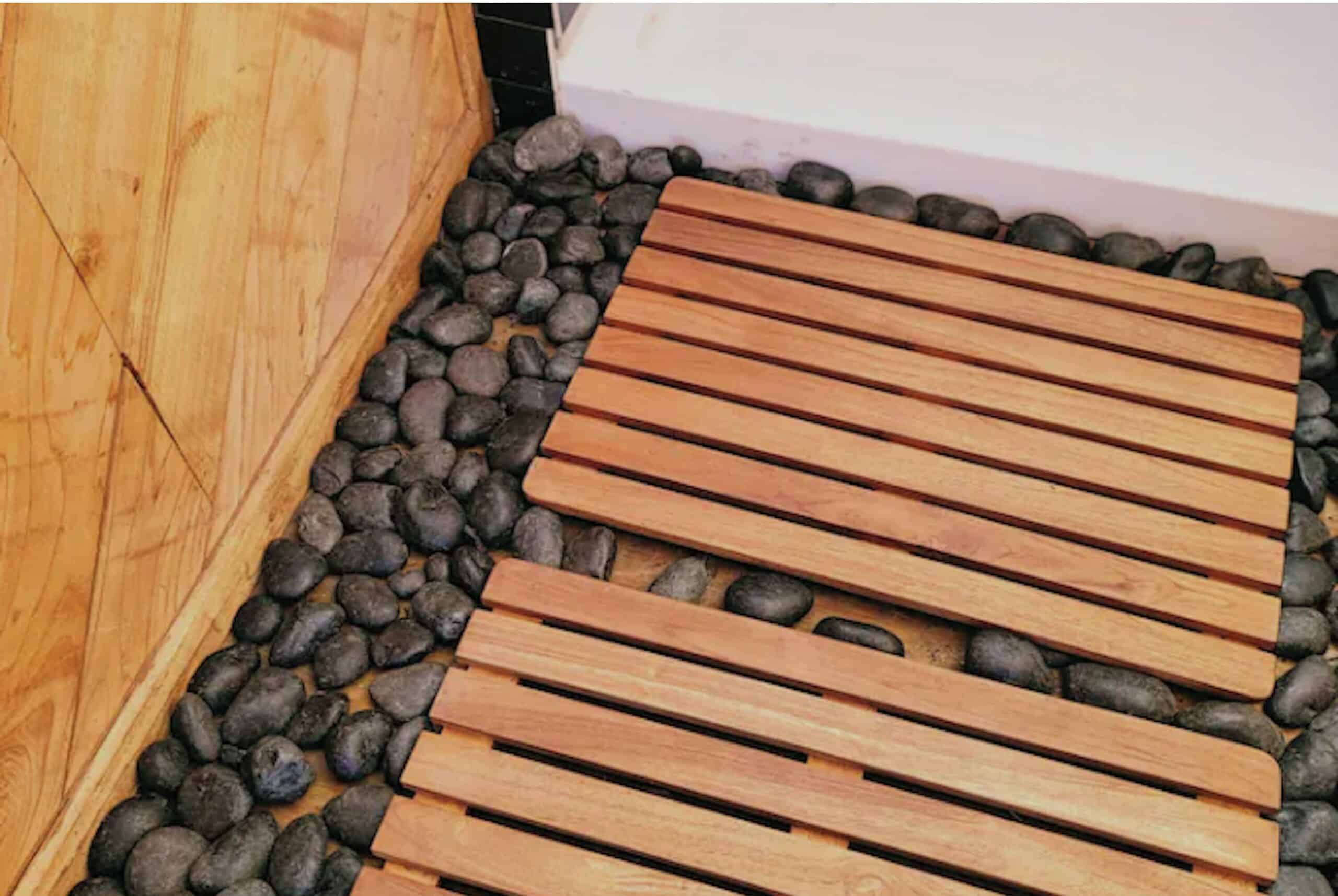 River rock and teak wood mat detail at the base of the outdoor shower