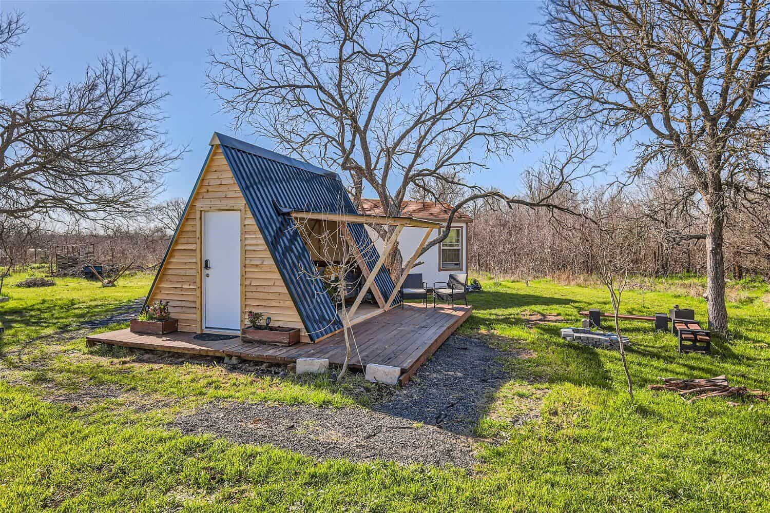 A-frame cabin exterior with blue metal roof, wood deck, and fire pit area on Texas countryside