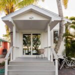 Small white cottage with front porch, surrounded by palm trees, in a tropical setting.