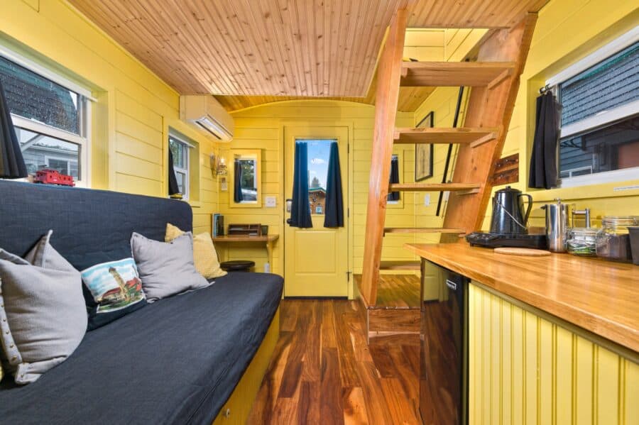 Couch bed, kitchen counter, and loft stairs inside the Arthur tiny house
