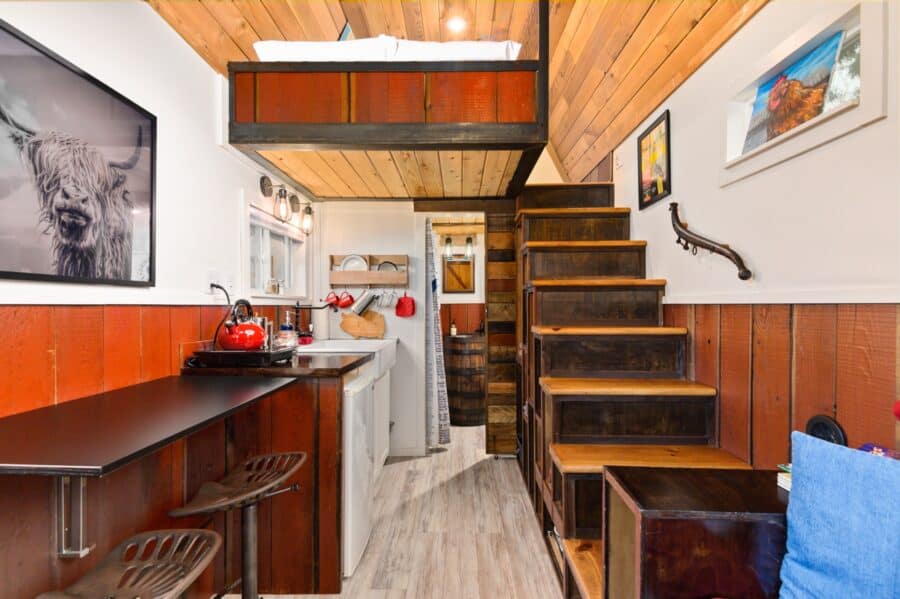 Interior of the Barn tiny house with drop-down dining counter, tractor seat stools, and loft stairs