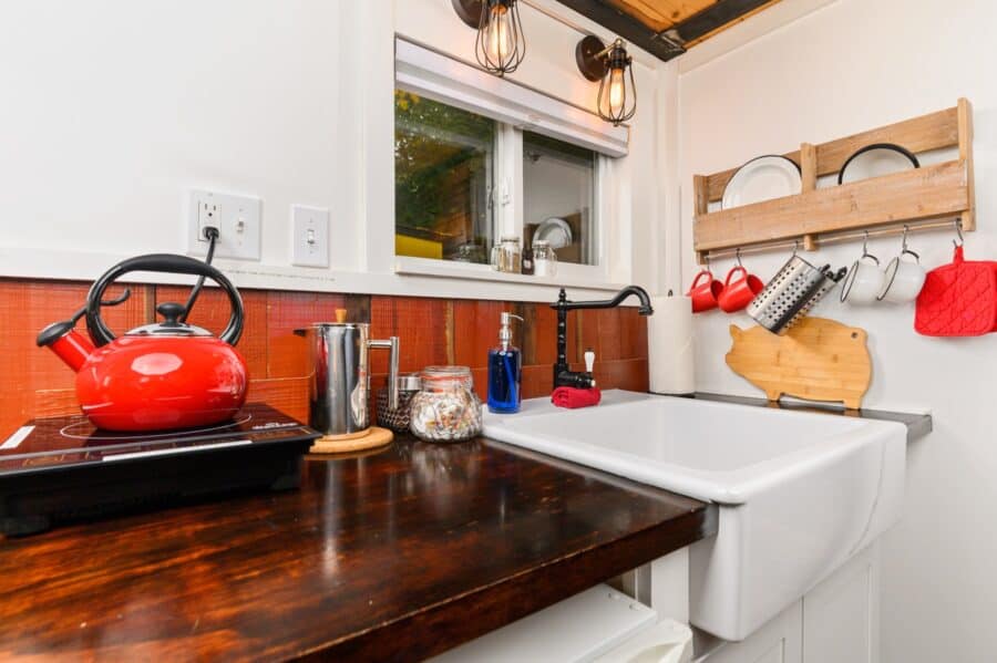 Farmhouse apron sink and red kettle in the kitchenette of the Barn tiny house